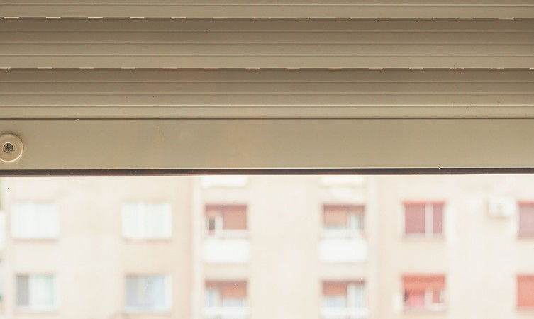 Cajón de persiana beige visto desde el interior de un piso de bloque, con la persiana recogida y el bloque de enfrente