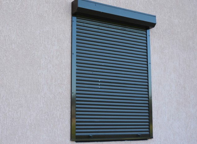 Persiana enrollable metálica lacada en verde con el cajón exterior visto sobre un muro liso
