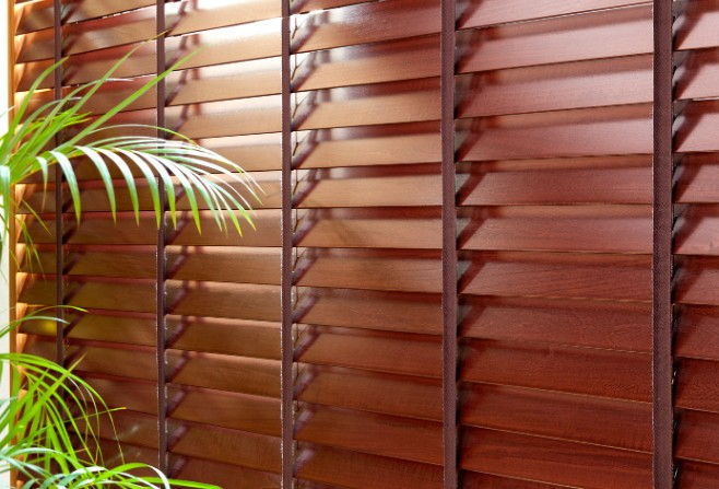 Venecianas de madera color caoba con cintas decorativas verticales y una planta de interior delante